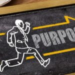 ”purpose”の文字と走る人が描かれたブラックボード